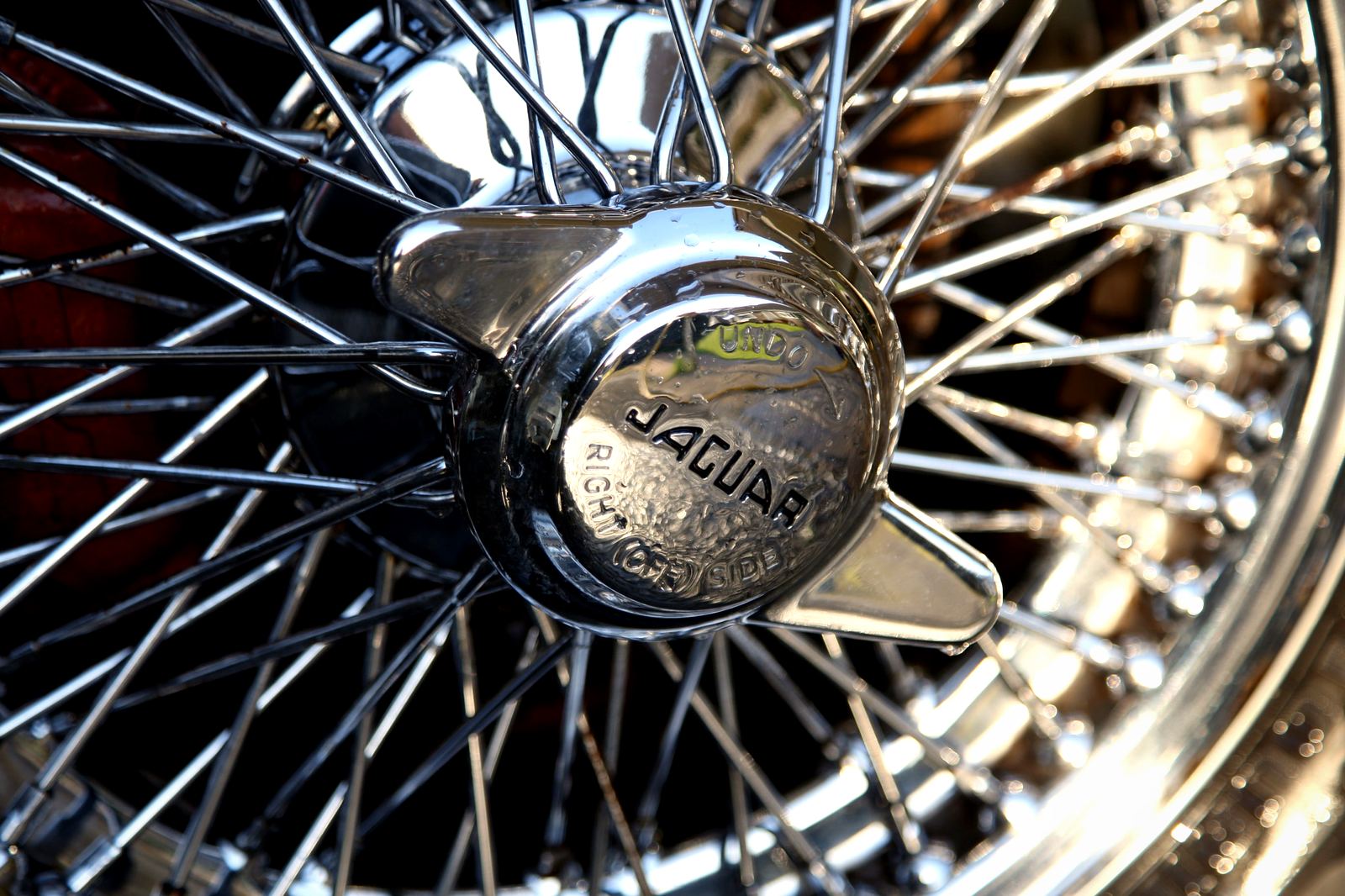 The chrome knock-off hub and wire spokes of a classic car wheel.