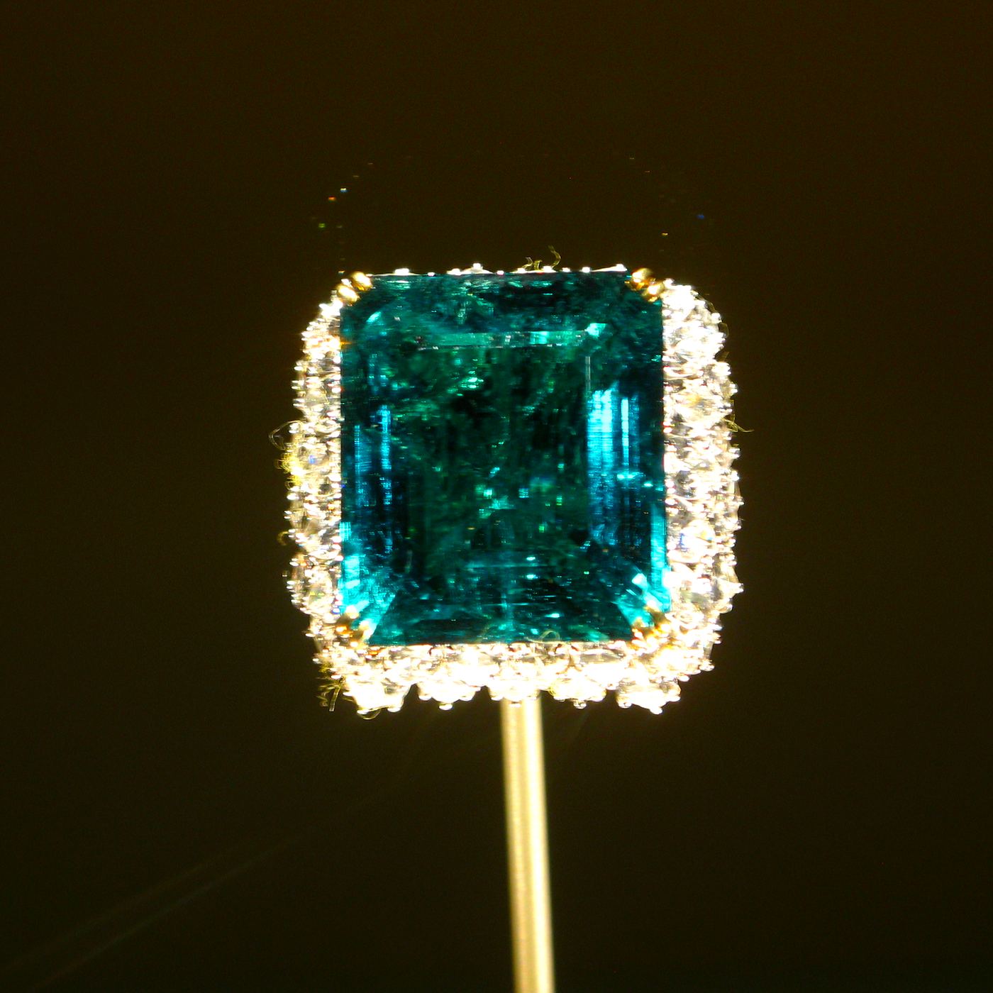 A large square-cut emerald framed in diamonds, lit against darkness.