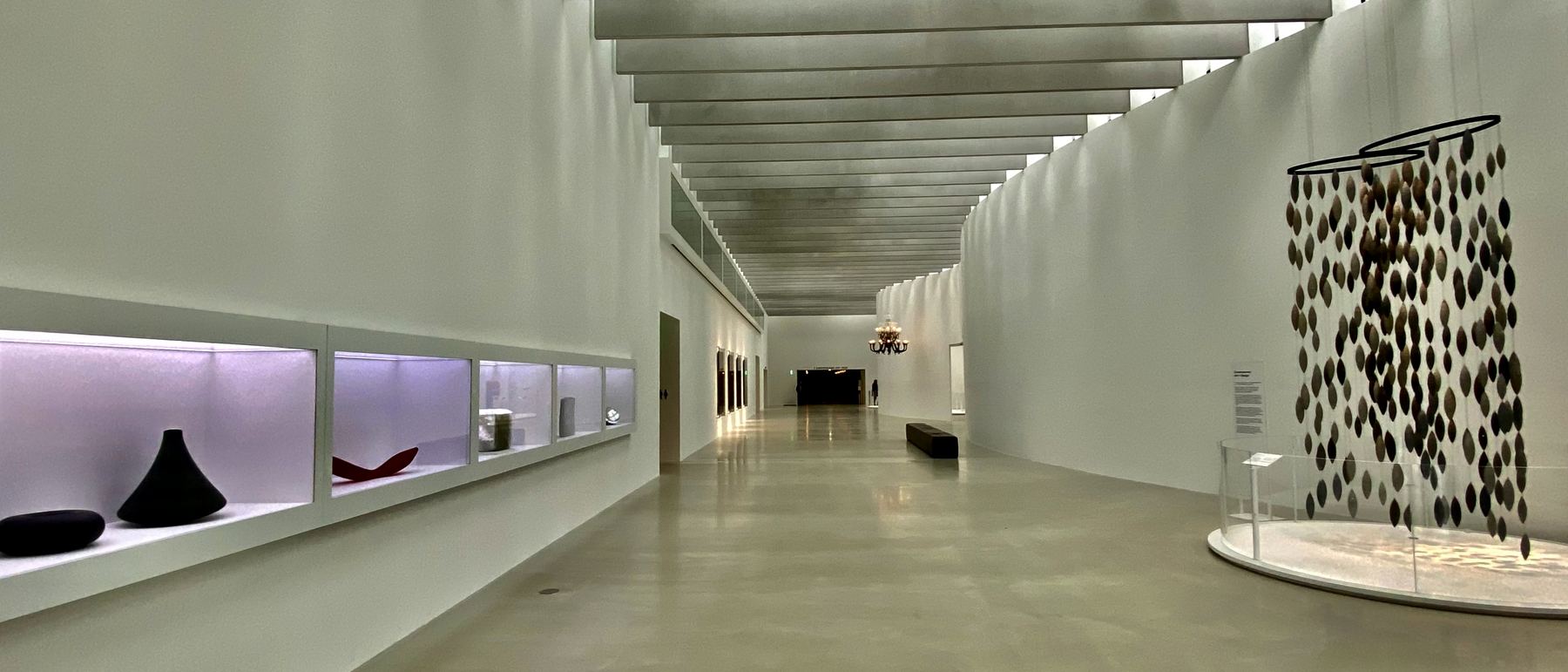 A long white gallery hall with sculptures in lit alcoves.