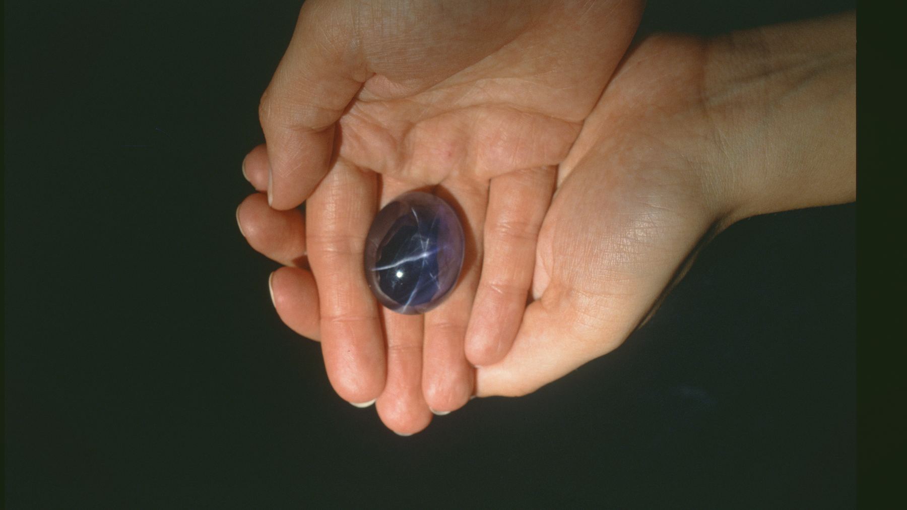 Two cupped hands holding a rough blue sapphire.