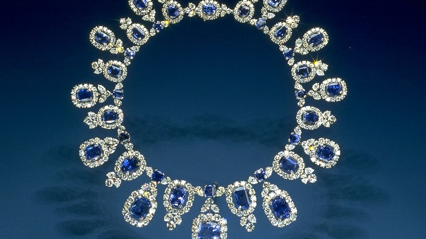 A sapphire and diamond necklace laid on blue velvet, photographed under studio light.